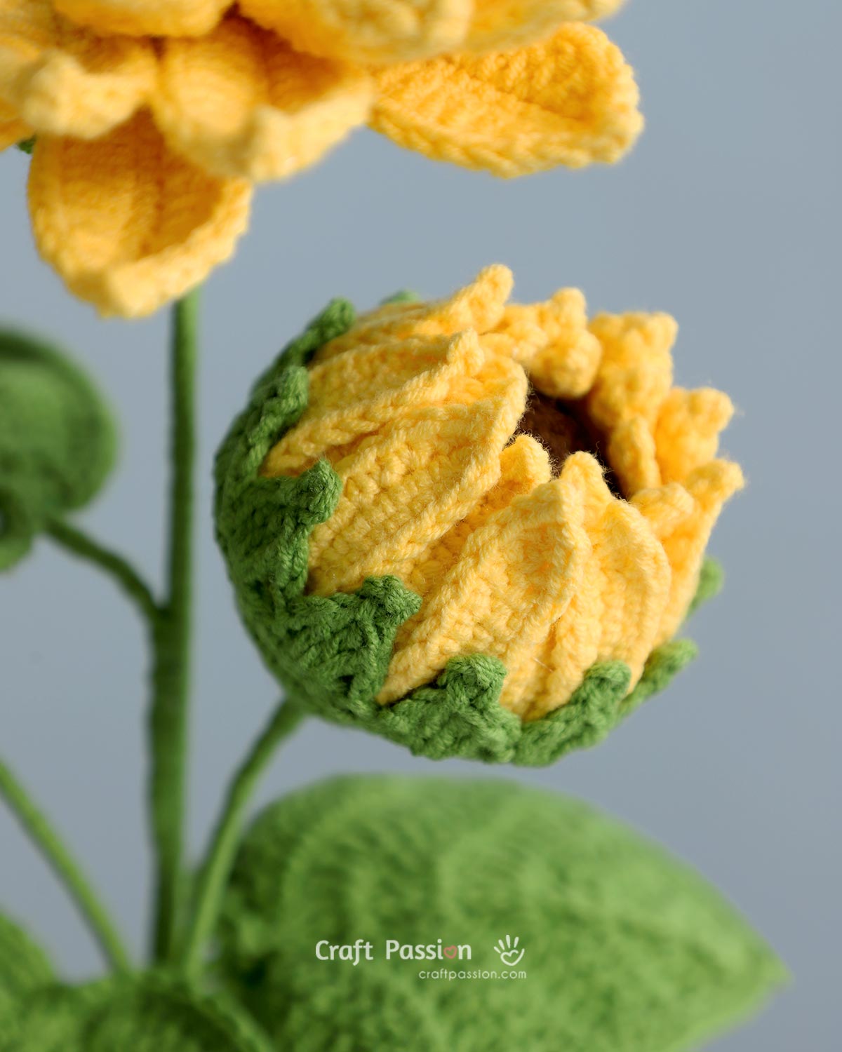 crochet sunflower bud pattern Opening crochet sunflower bud with yellow petals, brown center, and green sepals