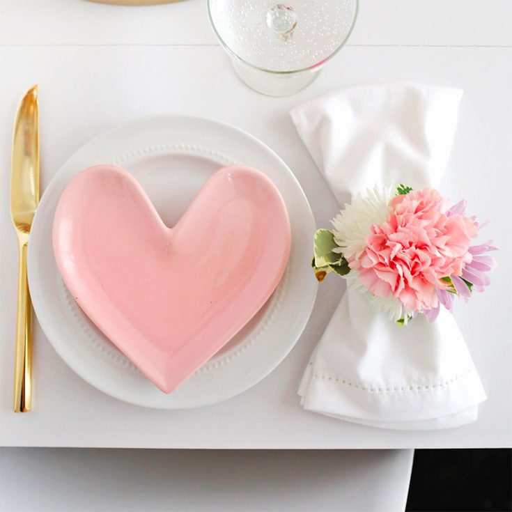 Up your Valentine's Home dinner by turning flowers she loves into a napkin ring. Add on other details like flowers in a vase and heart-shaped plates to match the occasion.