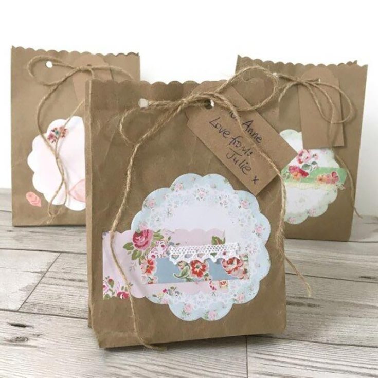 This elegant paper gift bag is decorated with cute patterns, stickers, ribbons, and lace for a personal touch. The scalloped top and twine closure add an extra bit of flair, making it a lovely handmade touch to your thoughtful gift!